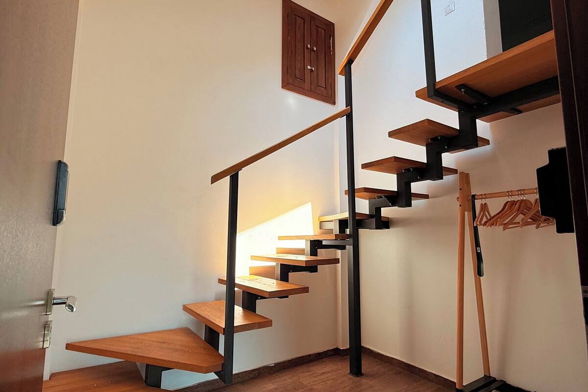 A modern staircase with wooden steps and metal railings, leading to a loft area with a skylight.