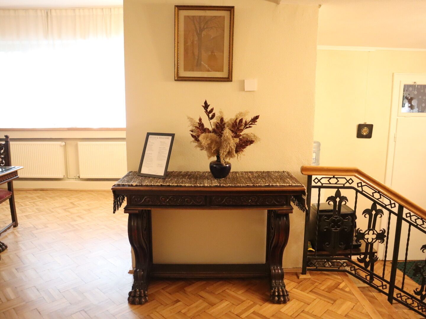 A wooden table with a vase of dried flowers, a framed picture on the wall, and a staircase with a wrought iron railing.