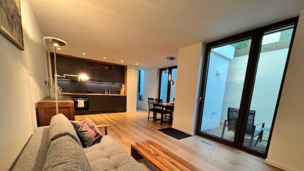 A modern living room with a grey sofa, wooden coffee table, and a kitchen in the background. - Apartment Ziegelhofring (Bad Vilbel)
