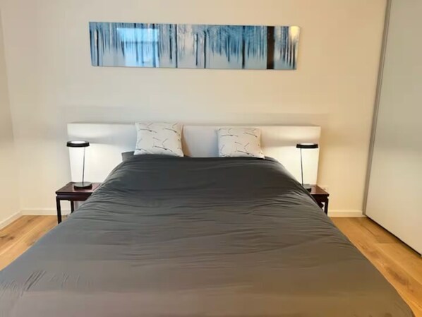 A bedroom with a large bed, two bedside tables with lamps, and a modern abstract painting on the wall. - Ziegelhofring Apartment (Bad Vilbel)