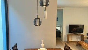 A dining area with a wooden table, chairs, a white vase, and a modern pendant light fixture. - Apartment Ziegelhofring (Bad Vilbel)