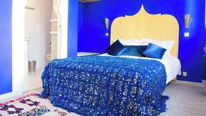 A bedroom with a blue wall, a wooden headboard, and a patterned bedspread. - Les portes de l'orient spa 1 Riad around the castles. (Tours)
