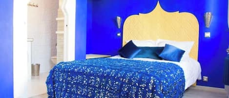 Un dormitorio con pared azul, cabecera de madera y colcha estampada.