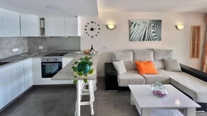 Een moderne keuken met witte kastjes, een centraal eiland en een eethoek met een witte tafel en stoelen.