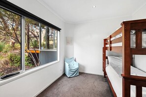 A bedroom with a bunk bed, a window with a view of trees, and a small wall-mounted picture. - Orchid Haven (Fairhaven)