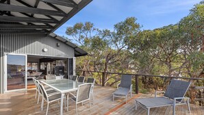An outdoor deck with a glass-top table and chairs, a covered seating area, and a view of the surrounding trees. - Orchid Haven (Fairhaven)