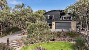 A modern two-story house with a garage, surrounded by a landscaped garden with various plants and trees. - Orchid Haven (Fairhaven)