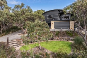 Une maison moderne à deux étages avec un garage, entourée d’un jardin aménagé avec différentes plantes et arbres.