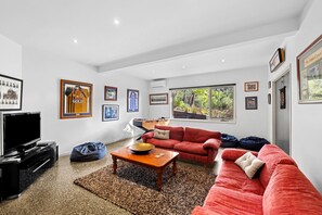 A spacious living room with a red sofa, a coffee table, a television, and framed sports memorabilia on the walls. - Orchid Haven (Fairhaven)