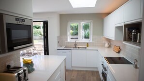 Una cocina moderna con armarios blancos, microondas integrado, tostadora y ventana con vistas a un jardín.