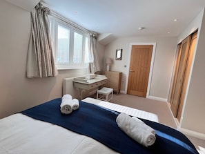 Een slaapkamer met een bed, een bureau, een stoel, een kledingkast en een raam met gordijnen.
