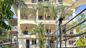 Un hotel de varios pisos con una escalera central, balcones y palmeras alrededor.