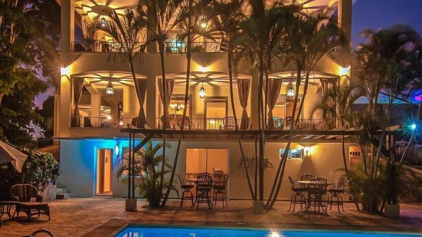 Un hotel de varios pisos con piscina, mobiliario exterior y palmeras.