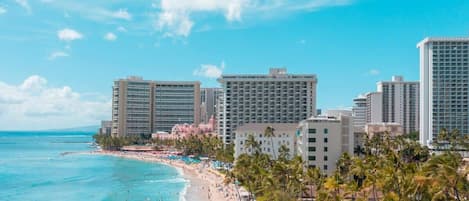 Un hotel frente a la playa con varios edificios altos, una playa de arena y palmeras.