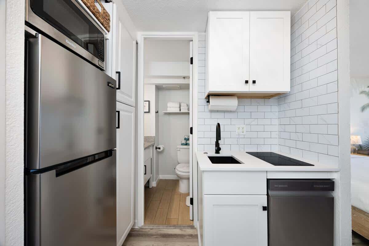 A compact kitchen with a stainless steel refrigerator, a dishwasher, and white cabinetry.