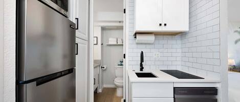 A compact kitchen with a stainless steel refrigerator, a dishwasher, and white cabinetry.