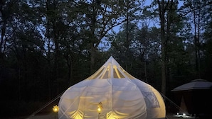 Tenda em forma de abóbada com plataforma e luzes, rodeada por árvores.