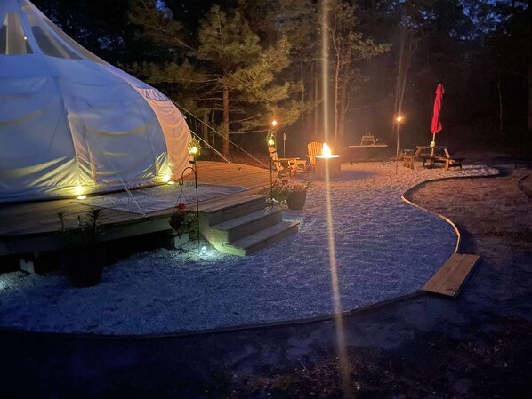 A tent with a wooden deck, a fire pit, and outdoor seating.