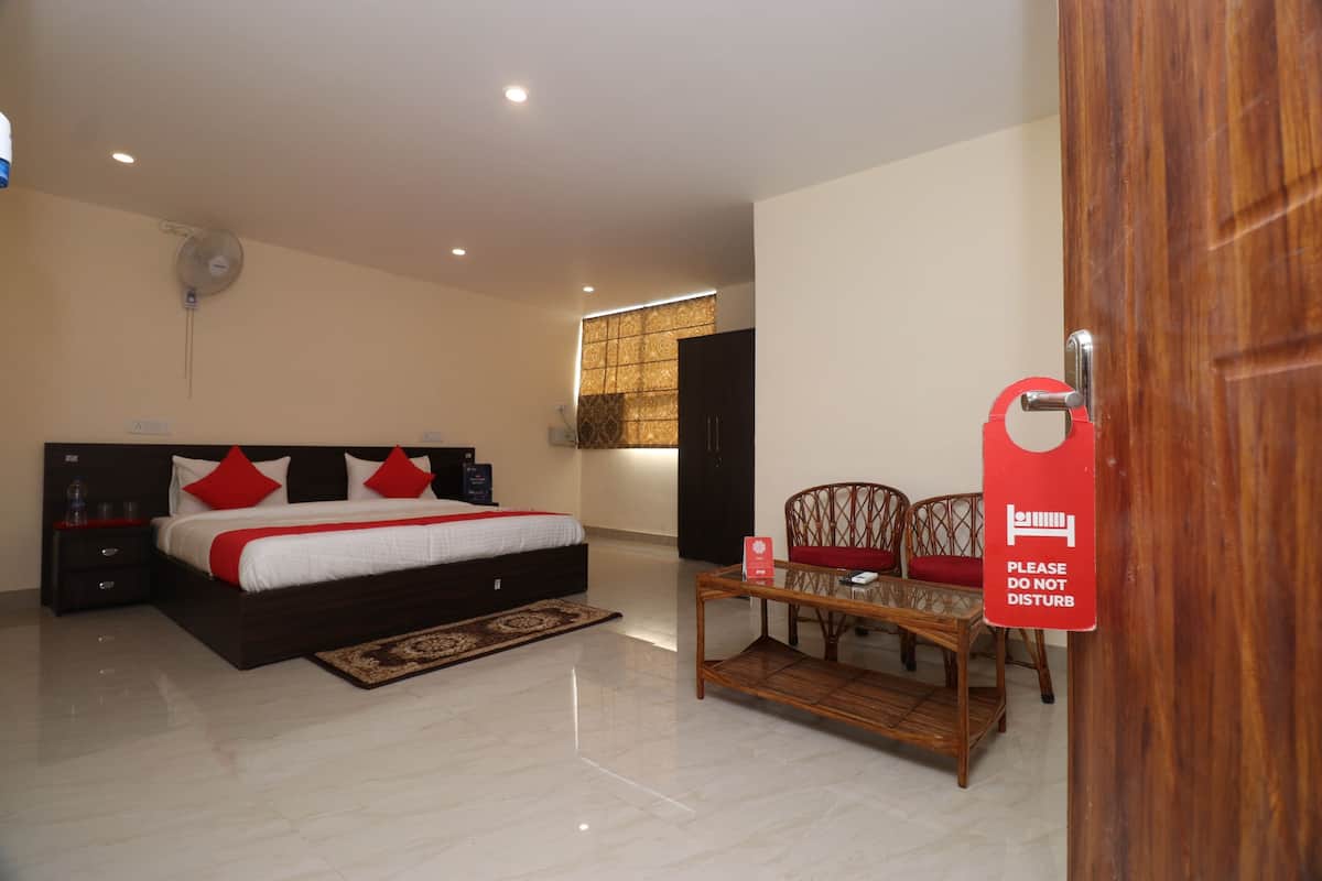 A hotel room with a bed, bedside tables, a small table, a chair, a wooden door, and a sign on the door.