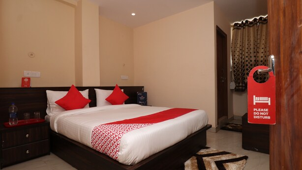 A hotel room with a large bed, two red pillows, a wooden headboard, a nightstand with a red tray, and a sign on the door. - HOTEL O MDA INN (Lucknow)