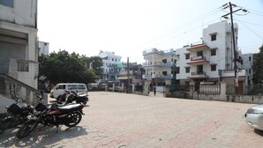 A paved street with parked motorcycles and a white van. Buildings line the street, and there are power lines overhead. - HOTEL O MDA INN (Lucknow)
