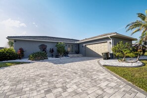 A single-story house with a garage, a paved driveway, and a landscaped front yard with various plants. - ‼️Punta Gorda Paradise‼️| 3BR w/ Water Views, Pool (Punta Gorda)