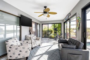 Una sala de estar moderna con ventilador de techo, caminadora y ventanas amplias que ofrecen vistas al exterior.
