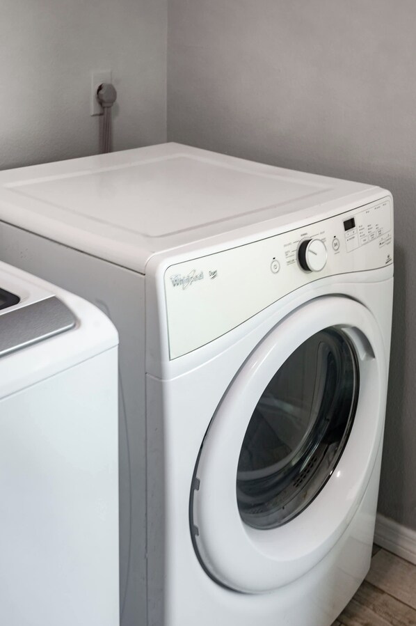 Una lavadora de carga frontal blanca con panel de control, un enchufe eléctrico montado en la pared y un piso de baldosas.