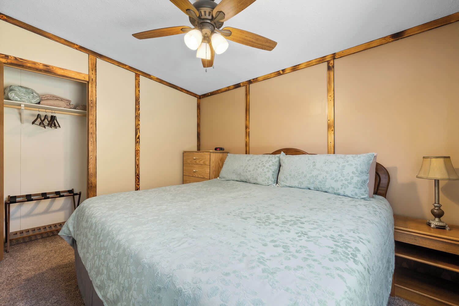Une chambre à coucher comprenant un lit, une armoire en bois, un ventilateur de plafond et une lampe de chevet.