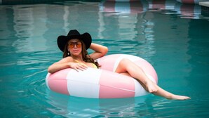 A person in a pool using a pink and white inflatable ring. - Downtown Austin Stay + On-site Dining, Pool & Gym (Austin)