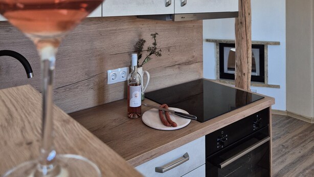 Una cocina moderna con armarios de madera, horno empotrado y una copa de vino sobre la encimera.