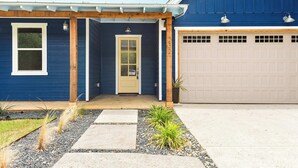 Una casa azul con una puerta de garaje color beige, una puerta principal y un pequeño porche con columnas de madera.