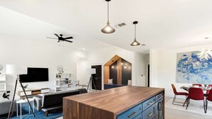 Un amplio salón con una isla de madera, ventilador de techo e iluminación colgante.
