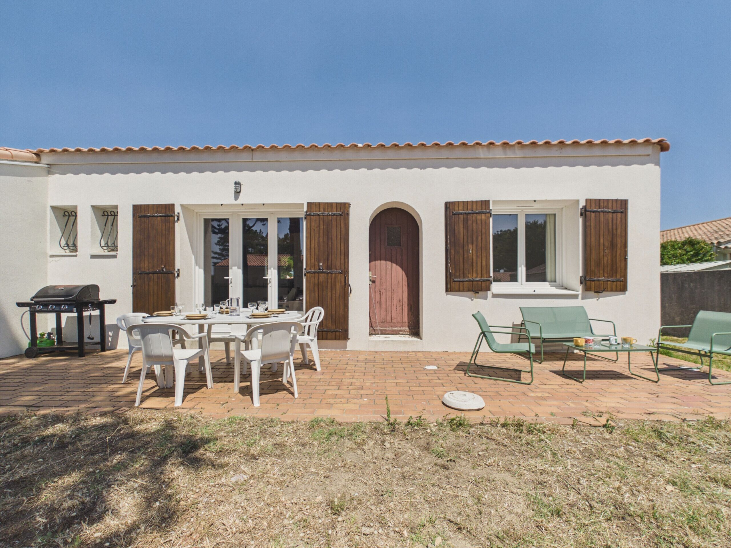 A house with a patio, a dining table with chairs, a barbecue grill, and a red door.