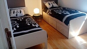 A bedroom with two beds, a bedside table with a lamp, and a wardrobe. - Gîte "aux nids d'hirondelles", 8 kms from the beach. (Hénansal)