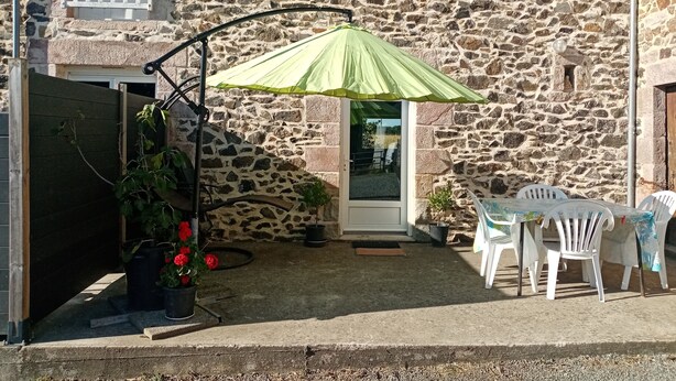 A stone building with a small patio area featuring a table and chairs, a green umbrella, and potted plants. - Gîte "aux nids d'hirondelles", 8 kms from the beach. (Hénansal)