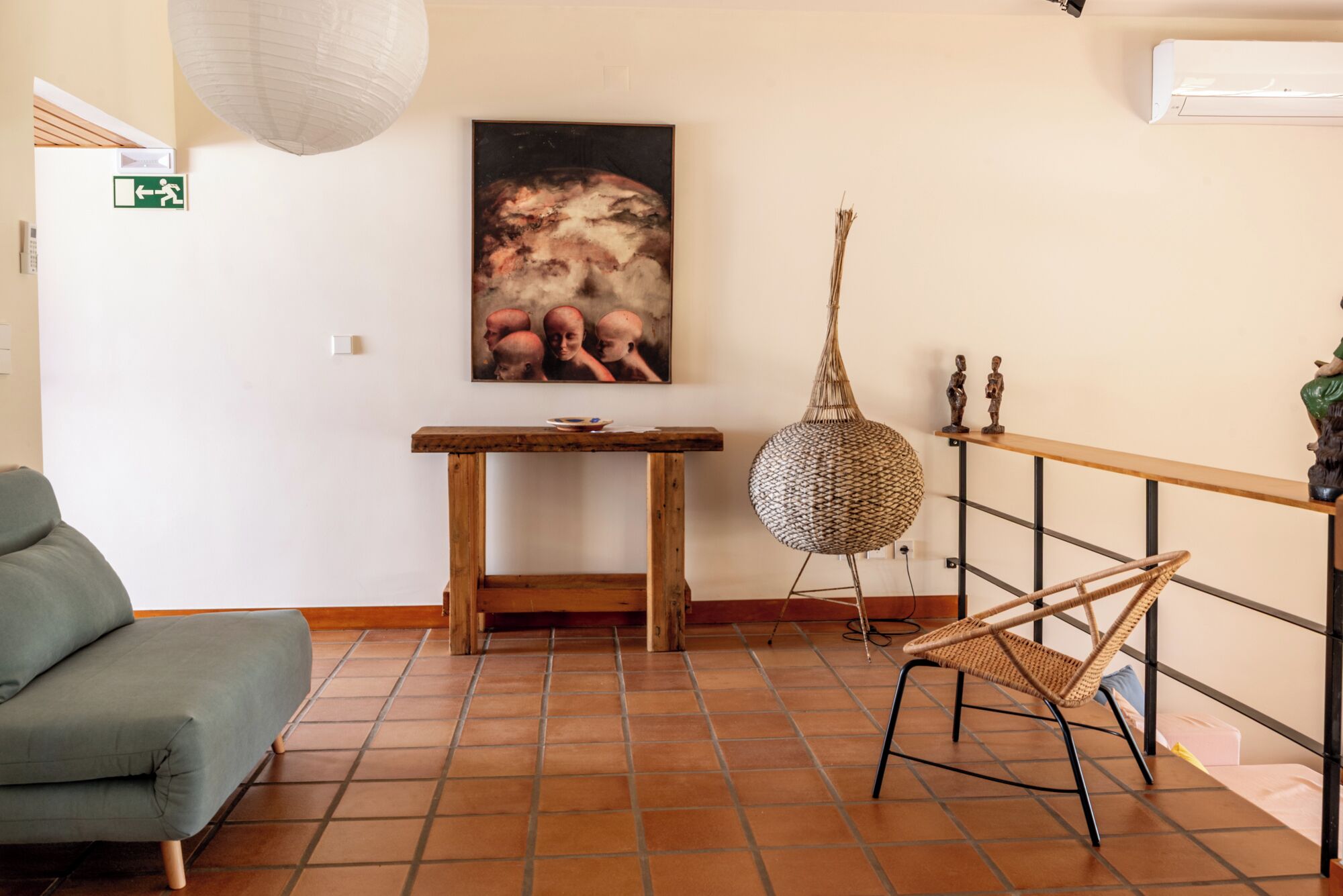 A room with a green sofa, a wooden table, a hanging lamp, and a painting on the wall.