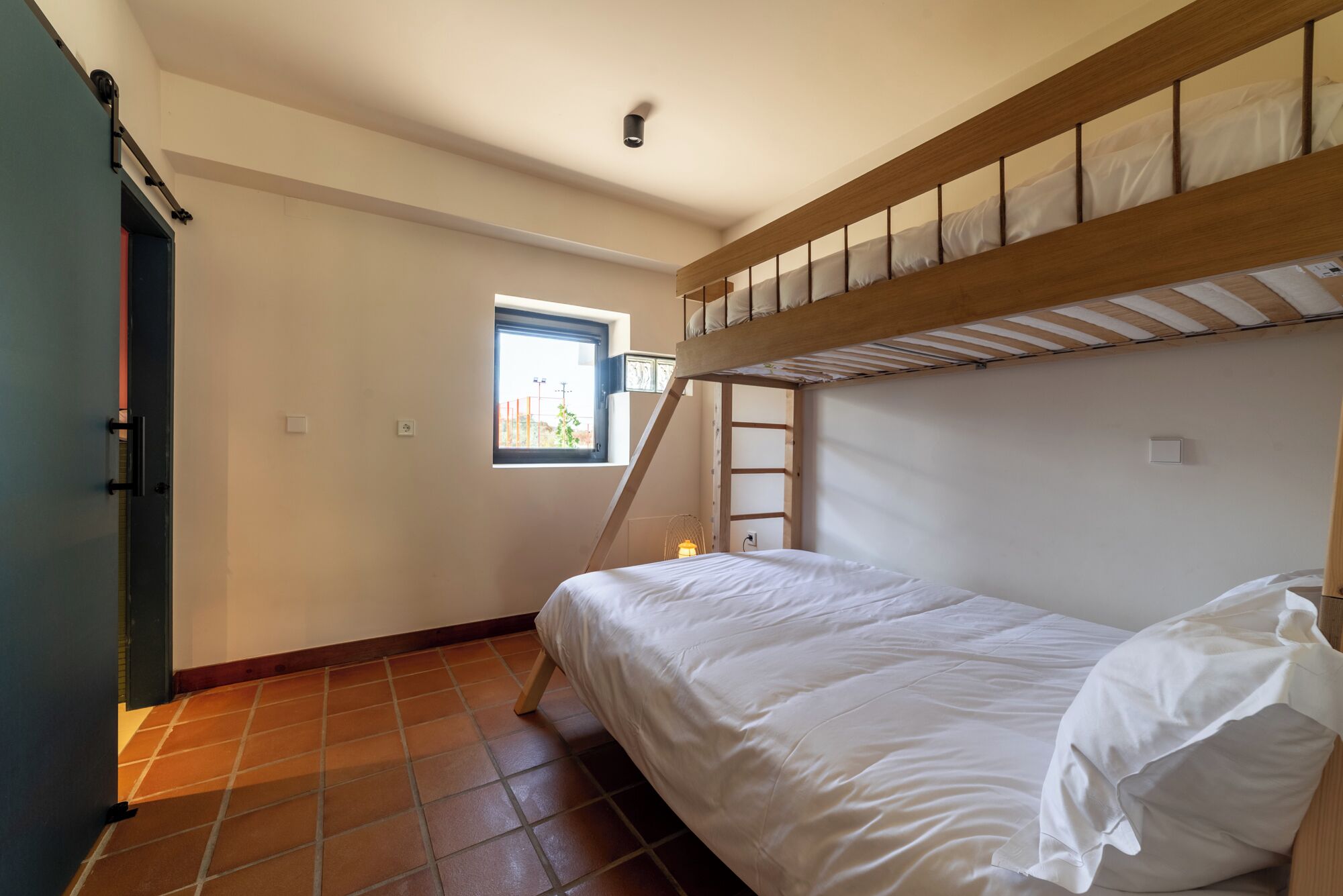 Een kleine kamer met een stapelbed, een klein raam en een deur.