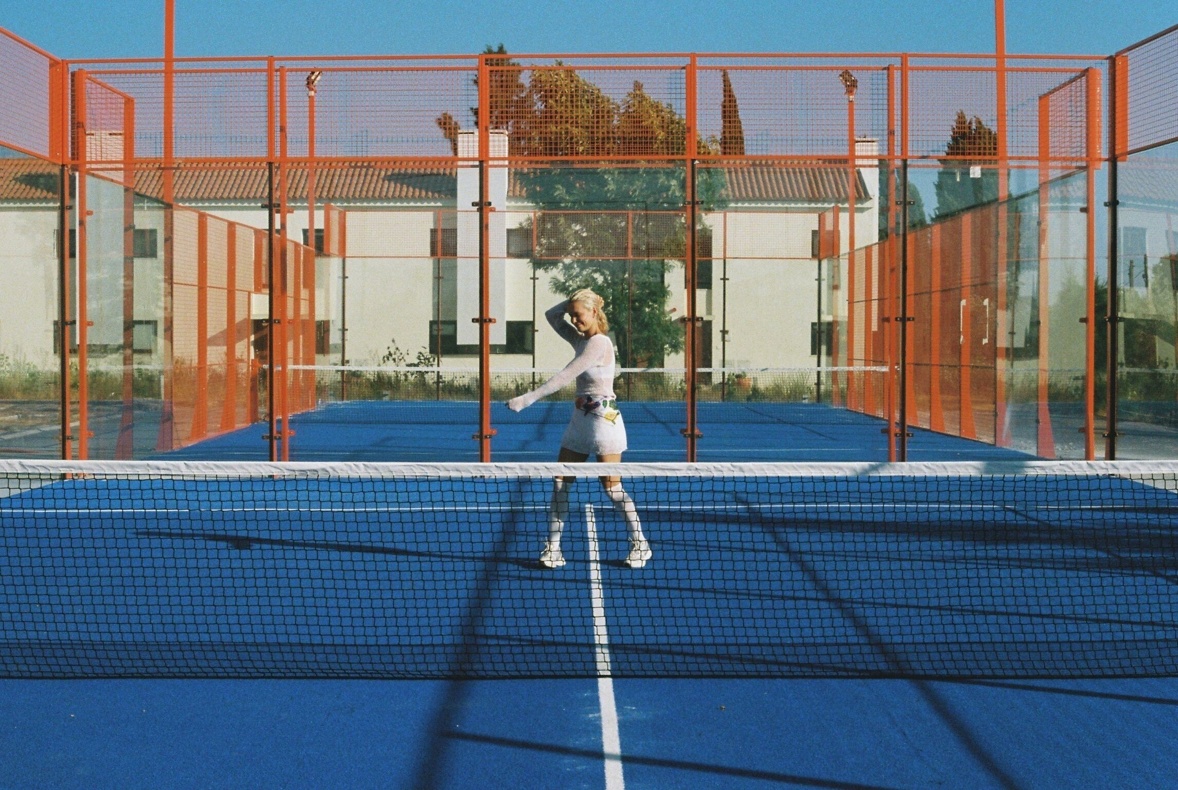 A tennis court with a net, surrounded by orange fencing.
