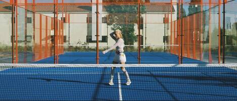 A tennis court with a net, surrounded by orange fencing.