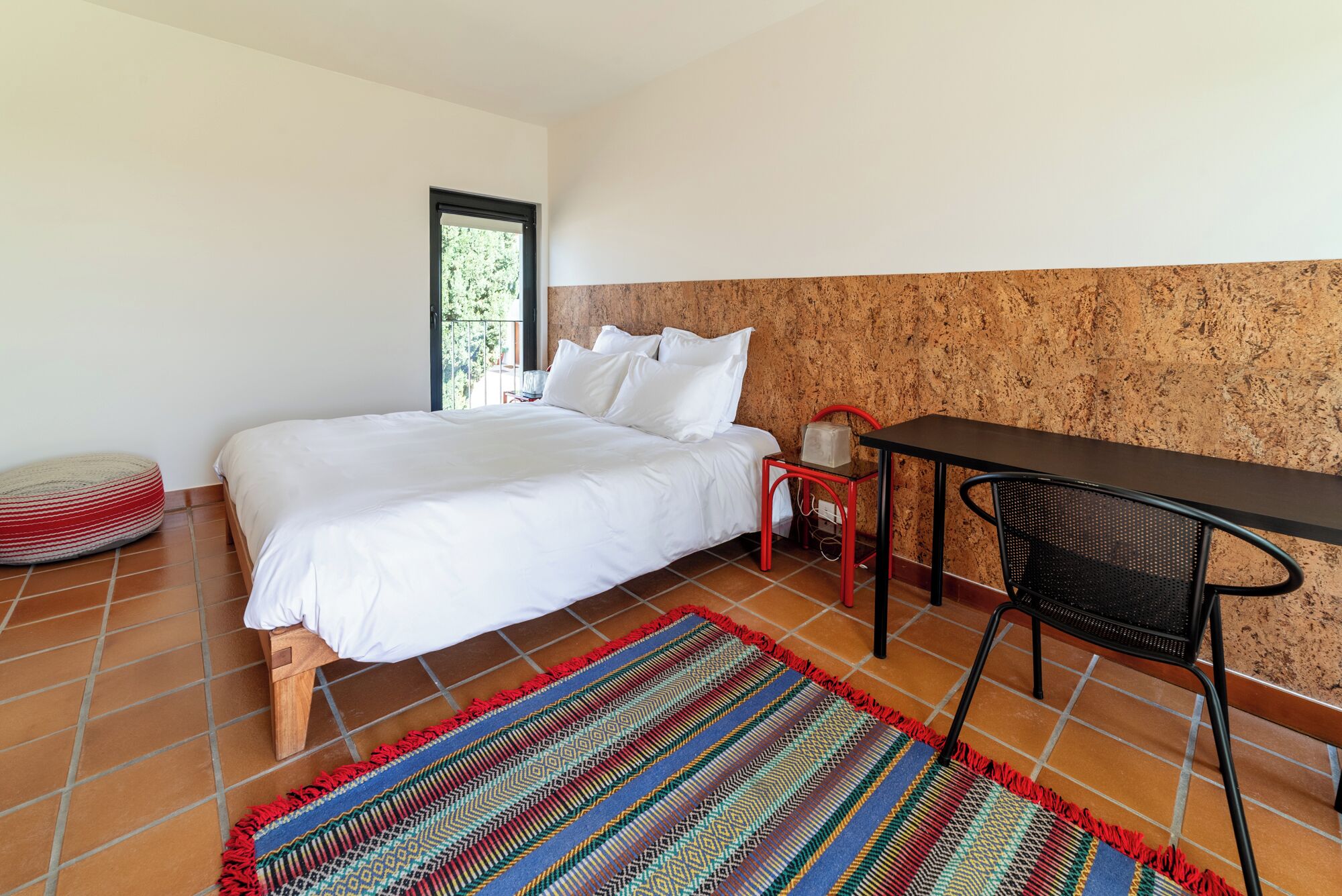 A bedroom with a bed, a small table, a chair, and a colorful rug.