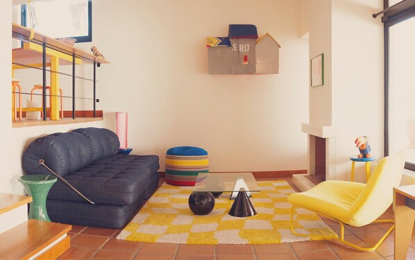 Una sala de estar con un sofá, una silla amarilla, una mesa de centro y un tapete estampado.
