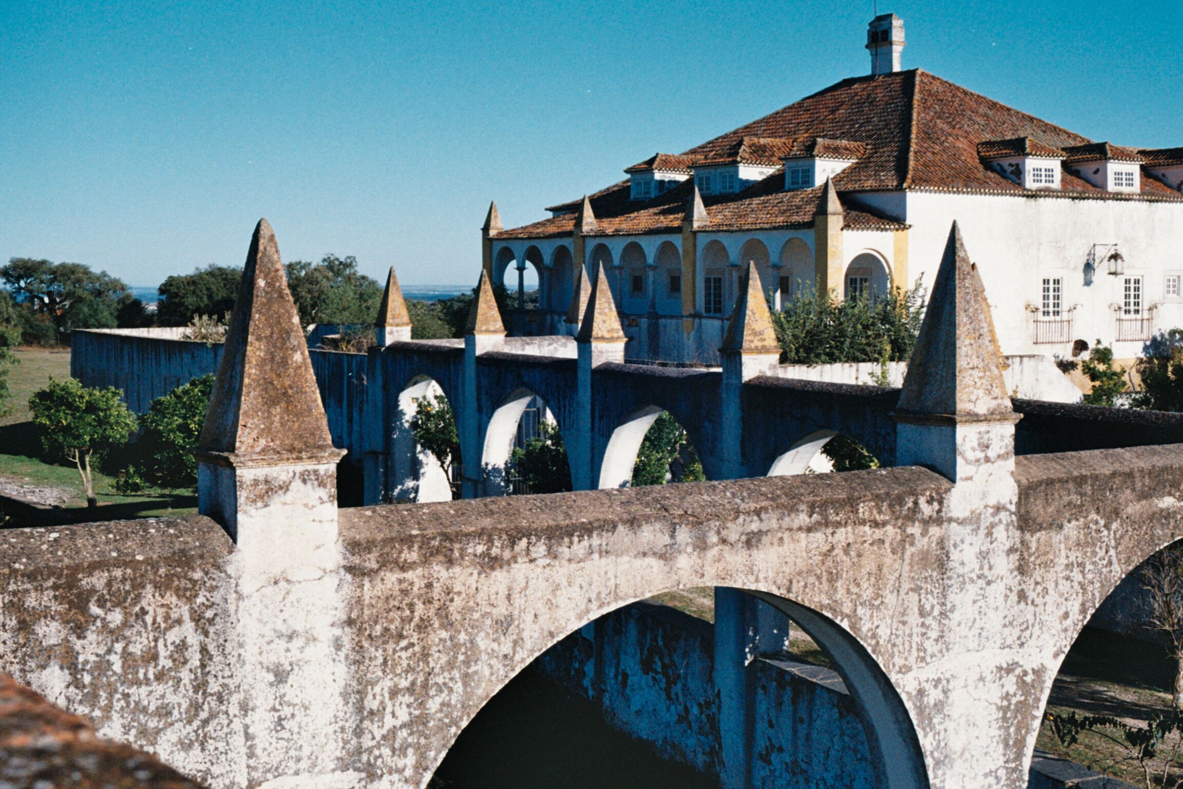 Un pont amb arcs i un edifici amb teules al fons.