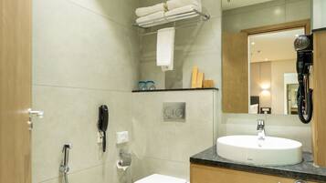 A modern bathroom with a sink, toilet, and shower. There is a towel rack with folded towels, a hairdryer, and a phone on the wall.