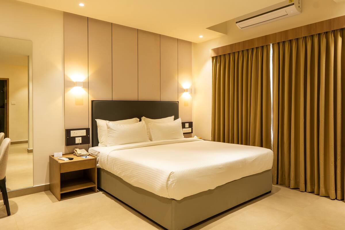 A modern hotel room with a large bed, bedside tables, a mirror, and a window with curtains.
