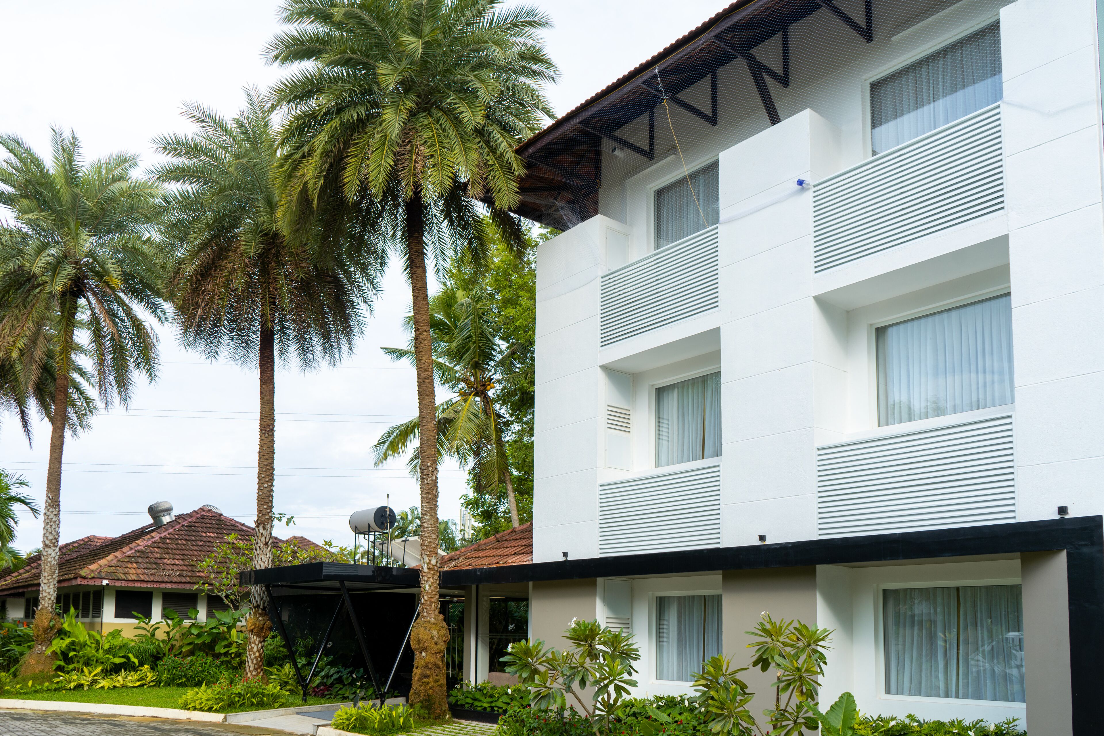 Een modern hotel met een witte gevel, meerdere balkons en weelderige tropische beplanting.