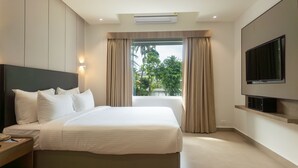 A hotel room with a large bed, a flat-screen TV mounted on the wall, and a window with curtains. - Riviera Garden (Kanayannur)