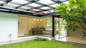A modern interior with a glass wall, a seating area, and a green plant. - Riviera Garden (Kanayannur)