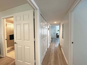 A hallway with white doors, a tiled floor, and a view into a bathroom with a towel hanging. - Anastasia by the Sea 208A – Where Plans Meet Possibilities (St. Augustine)