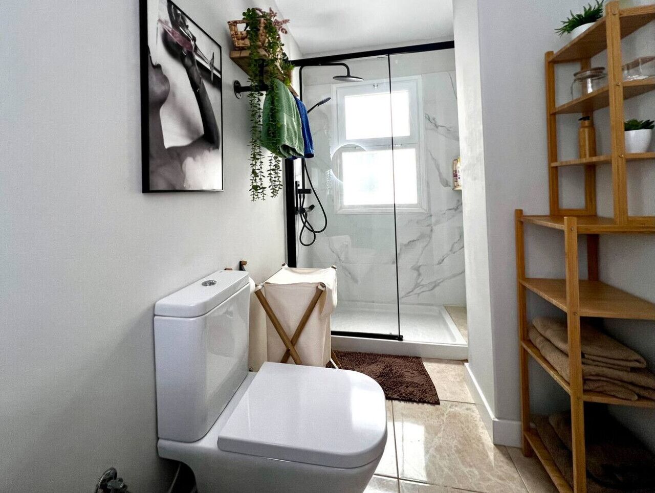 Une salle de bain moderne équipée de toilettes, d’une douche et d’une étagère en bois où sont rangées les serviettes.